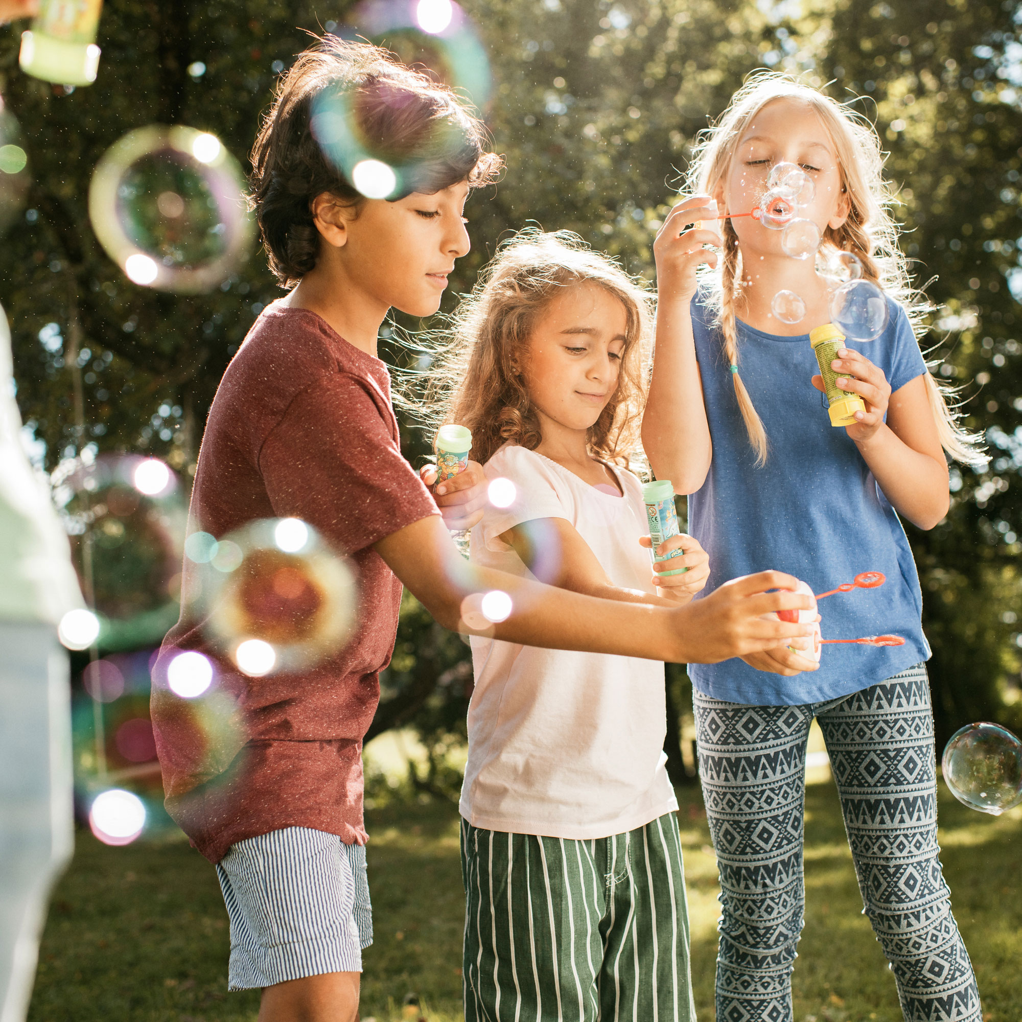 Tre barn blåser såpbubblor i trädgården en sommardag